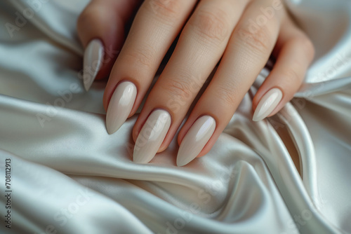 Closeup to woman hands with elegant neutral colors manicure on long almond shaped nails. Female hands with luxury nude shade nail manicure with gel polish on white silk background