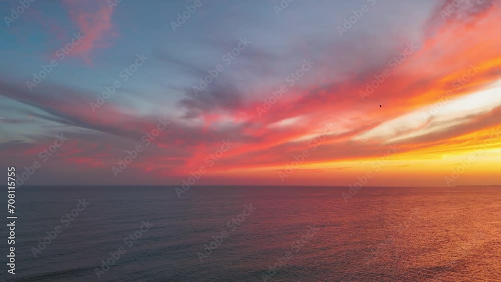Vibrant colorful sunset clouds over the ocean in Portimao. Flock of seagulls flying away