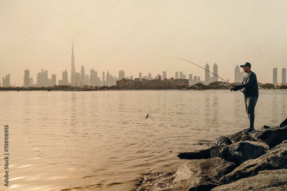 Man cought a fish from the rocks with the Dubai skyline on the background