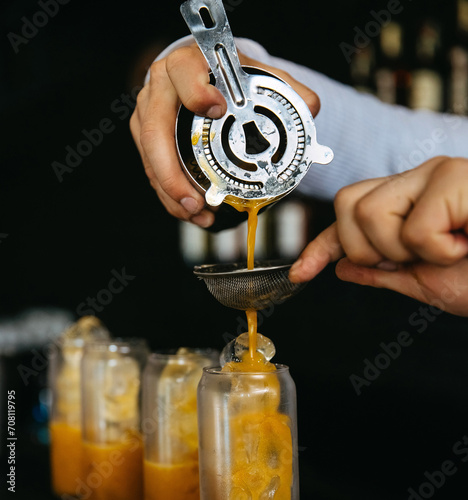 Photography Bartender pouring an orange drink through a strainer into a glass