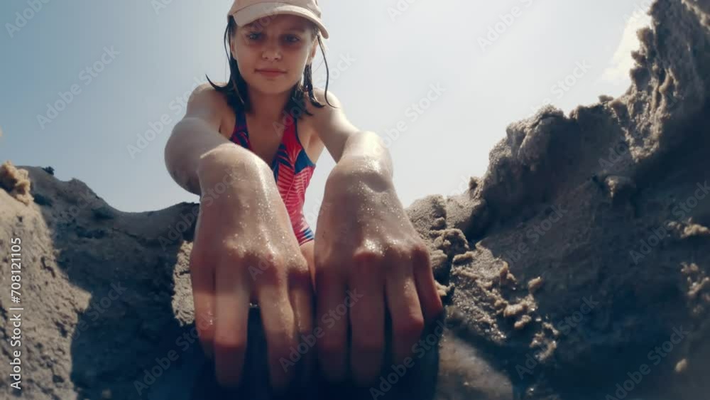 Girl child digging hole in sand at beach and making video with smartphone. Pretty kid playing at sea coast at summer holidays