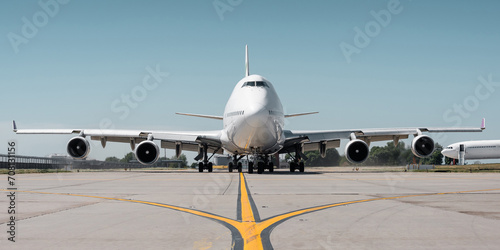 Huge white passenger aircraft taxiing on a sunny day, hot exhaust coming out of the engine and distorts the visibility. Frontal symmetric view of two-storey jumbo jet on a ground.