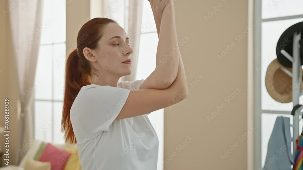 A serene redhead woman stretching in a sunlit living room, exuding calm and wellbeing. A serene redhead woman stretching in a sunlit living room, exuding calm and wellbeing.