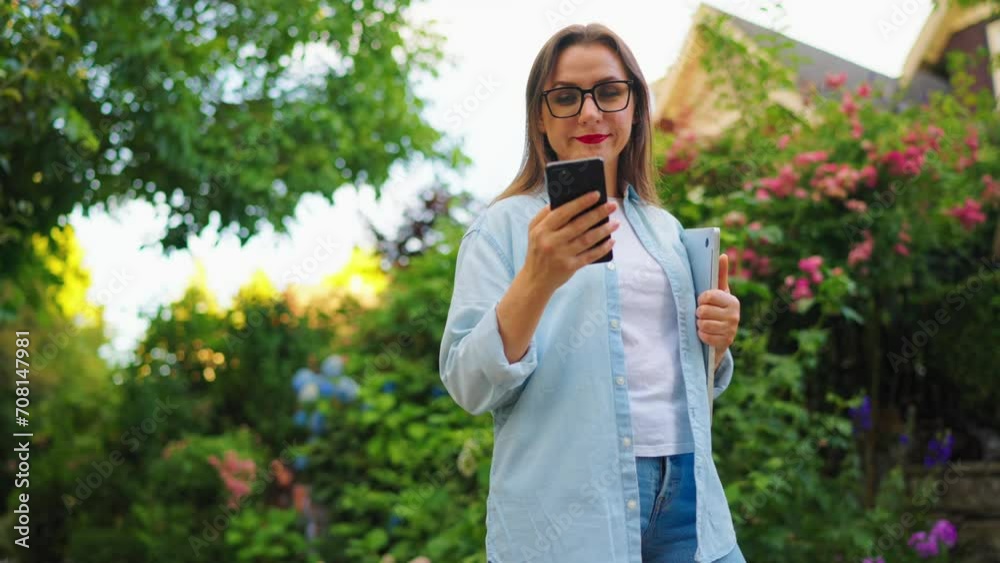 Woman with laptop and smartphone standing in the blooming garden Woman with laptop and smartphone standing in the blooming garden