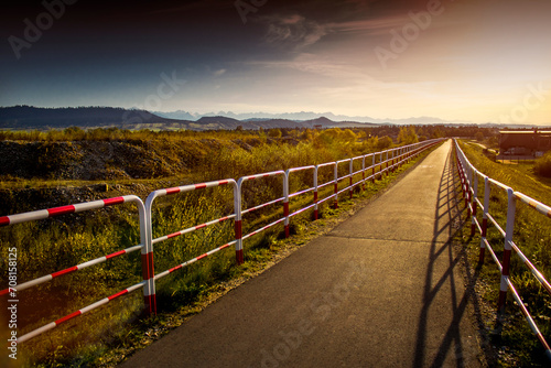 Ścieżka rowerowa z barierkami ochronnymi w dzikiej przyrodzie, na tle gór. Droga dla rowerów o zachodzie słońca.