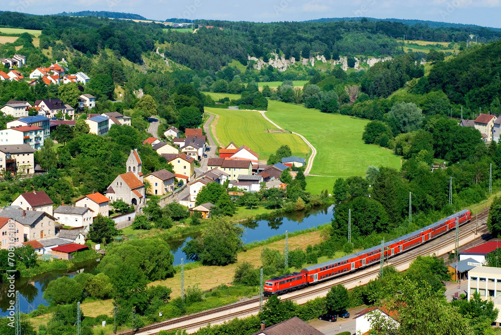 Altmühltal, village of Solnhofen, red train, green meadows, landscape, river Altmühl and rock formation of twelve Apostles in background,  Bavaria, Germany, Europe