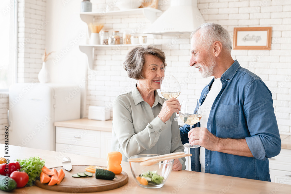 Old elderly senior couple grandparents spouses cooking together, drinking wine, toasting cheering while celebrating special event at home kitchen Old elderly senior couple grandparents spouses cooking together, drinking wine, toasting cheering while celebrating special event at home kitchen