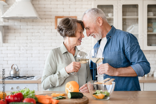 Romantic dinner date concept. Quality time - love language. Caucasian senior couple grandparents celebrating special event anniversary together  cooking and drinking wine at home kitchen