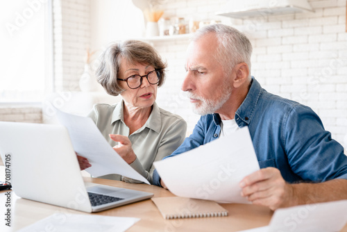 Concentrated concerned european senior old elderly couple spouses grandparents doing paperwork, paying domestic bills, rentals, receiving pension, calculating funds and budget at home kitchen photo