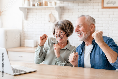 Caucasian senior old elderly couple husband and wife spouses grandparents watching movie, celebrating, winning, victory, cheering the prize from bidding online casino bets with laptop photo