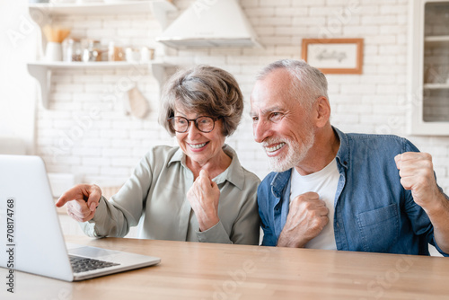 Receiving money, prize. Celebrating victory in lottery, online casino bets. Caucasian old senior couple using laptop for videocall with grandparents photo