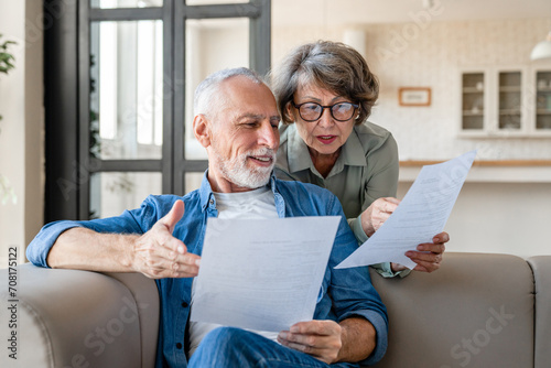 Mortgage loan debt transactions paying bills and documents. Caucasian senior old couple spouses reading marriage contract, doing paperwork, dealing with data at home photo
