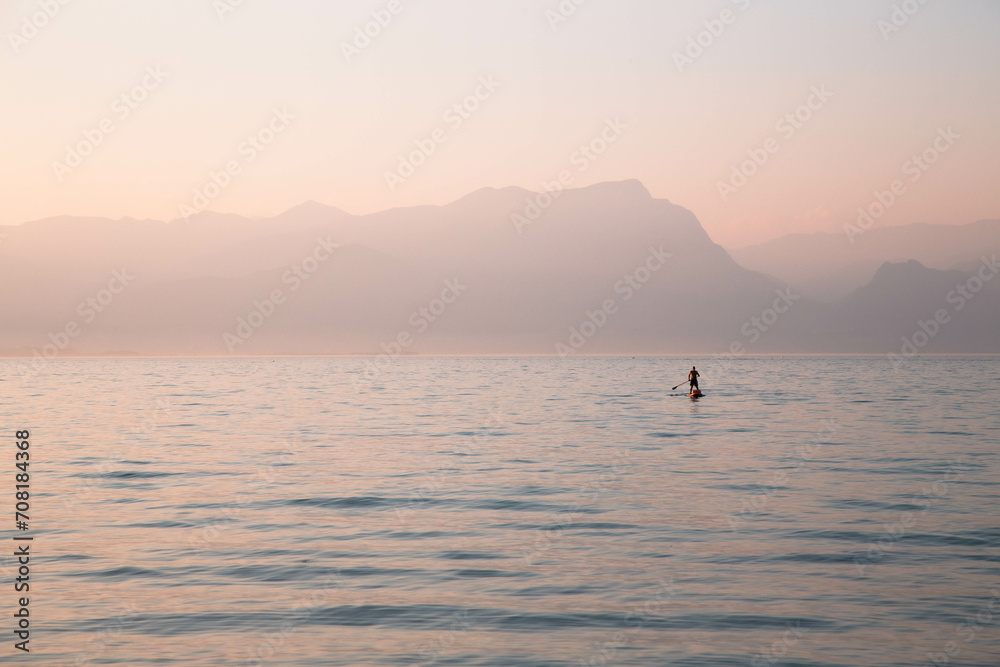 A lonely man standing on an inflatable board with an oar against a backdrop of misty mountains and a lake A lonely man standing on an inflatable board with an oar against a backdrop of misty mountains and a lake