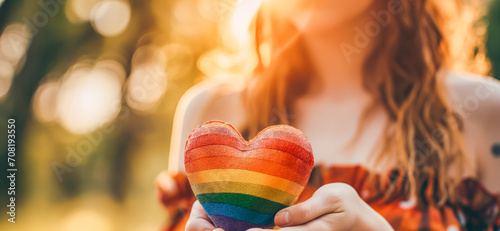 Woman holds in hands a heart in the colors of the rainbow. Young beautiful girl. LGBT history month. Pride Month. Lesbian Gay Bisexual Transgender.