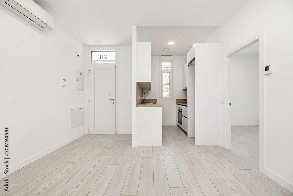 A loft-type home with light wooden floors, a small furnished kitchen and the rest of the rooms empty