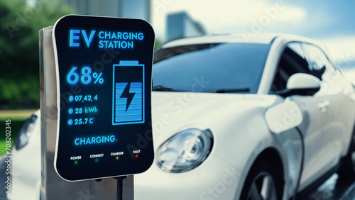 Electric car plug in with charging station to recharge battery with electricity by EV charger cable in eco green city park. Future innovative EV car using alternative clean energy reducing CO2. Peruse