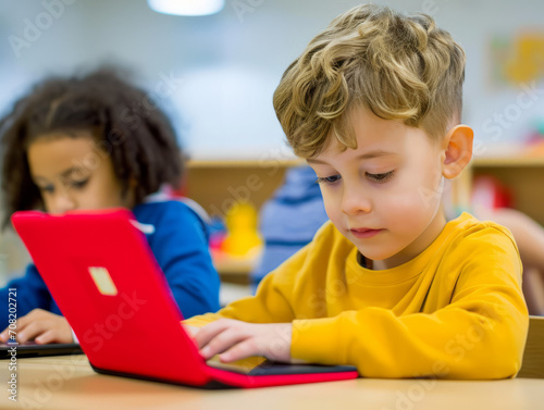 Cute little boy using a laptop in a classroom. Cute preschool child using a laptop computer. photo