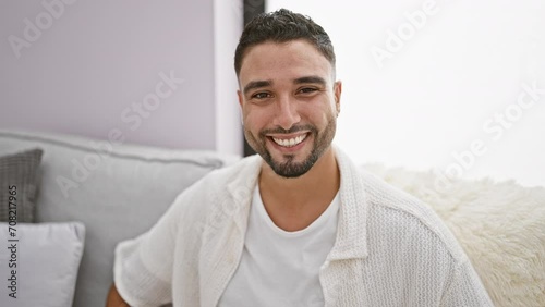 Cheeky young arab man perfectly winking at camera, giving a sexy wink from his living room sofa. his happy face beacons joy while oozing handsome charm, inducing laughter. home never looked this cool! photo