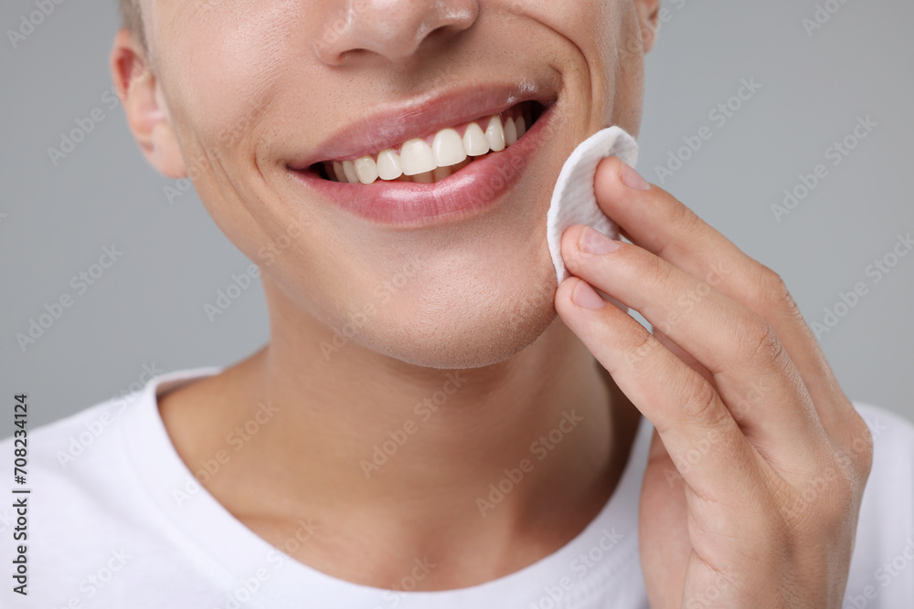 Obraz premium Man cleaning face with cotton pad on grey background, closeup