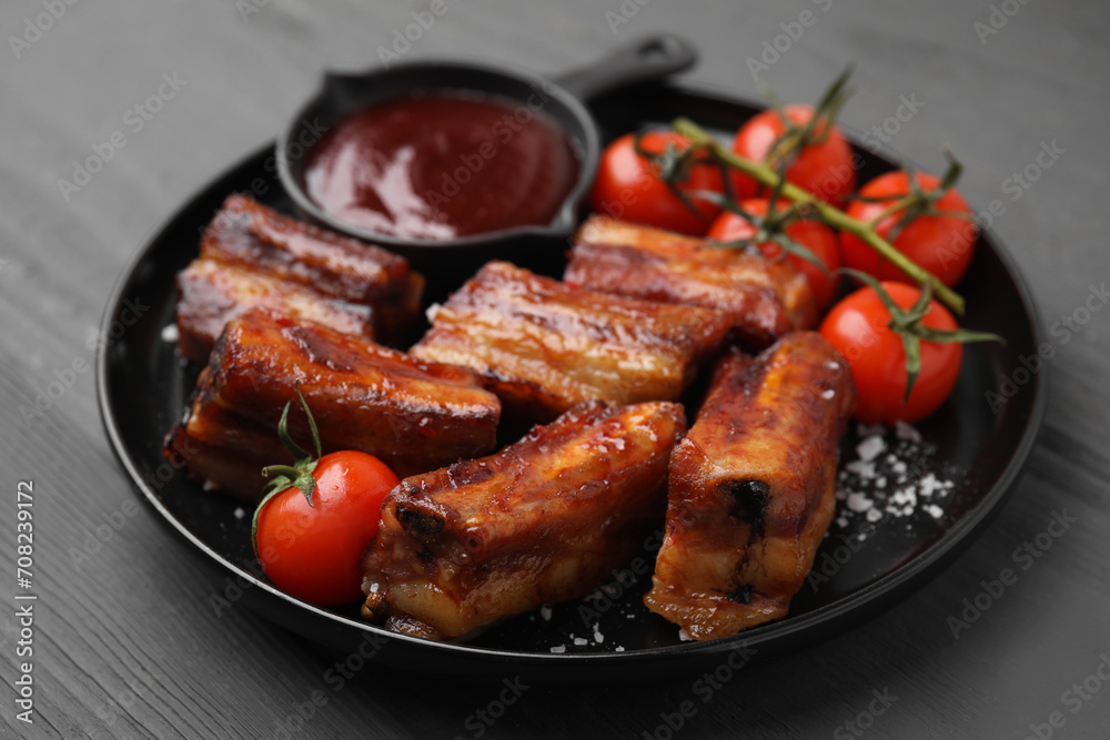Tasty roasted pork ribs served with sauce and tomatoes on grey wooden table, closeup Tasty roasted pork ribs served with sauce and tomatoes on grey wooden table, closeup