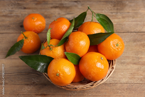 Delicious tangerines with leaves on wooden table, above view