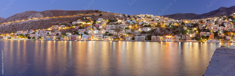 Multi-colored facades of houses in the light of lanterns in the village of Symi at sunset.