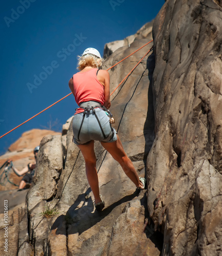 Looking up at a female rock climber repelling down a steep rock face against a blue sky