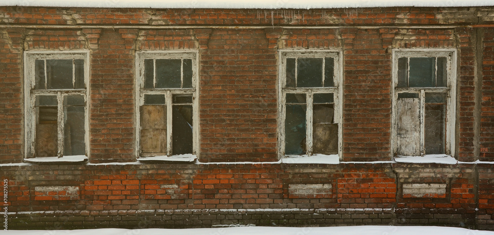An old brick wall of an apartment house with a lot of boarded up windows without glass