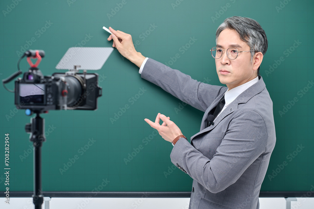 A middle-aged man is wearing a suit and giving a lecture in front of the camera pointing to the blackboard. A middle-aged man is wearing a suit and giving a lecture in front of the camera pointing to the blackboard.