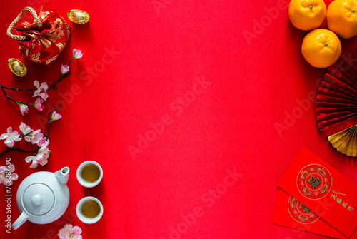 Chinese new year background concept with tea set, ingots(word means wealth), red bag, oranges and red envelope packets or ang bao(word means blessing and 5 blessing) on red satin cloth background.