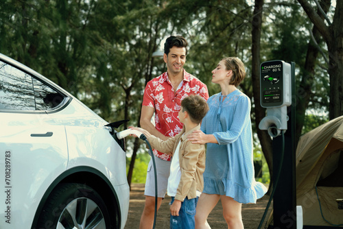 Outdoor adventure and family vacation camping in nature travel by eco friendly car for sustainable future. Lovely family recharge EV car with EV charging station in campsite. Perpetual photo