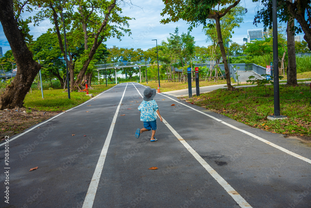 Little boy walking on city park pathway green tree forest