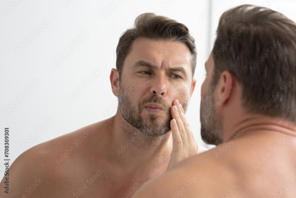 sexy man with stubble looks at the wrinkles on his face. Close up man looking in mirror, sensitive skin, cosmetology treatment. Skin care. joyful, virile, manly, attractive, naked, unshaven, handsome