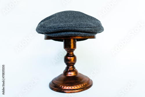 Detail of a scaly hat or flat cap or made of tweed herringbone mounted on a bronze mannequin head on a white background. Catalog photo of a classic dark gray hat on an elegant bronze mannequin photo