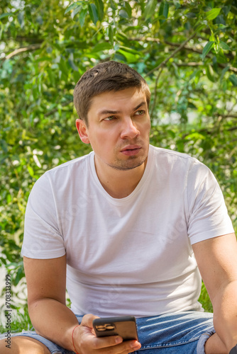 A thoughtful young man with a smartphone in his hand against the background of nature. Combining leisure and work