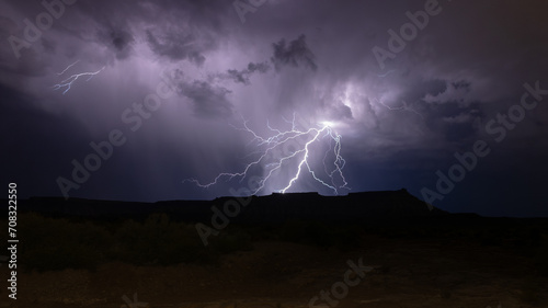 Threads of lightning spread out from the dark purple storm clouds above Gooseberry Mesa in Southern Utah like roots from a tree reaching down to the surface of the earth. 