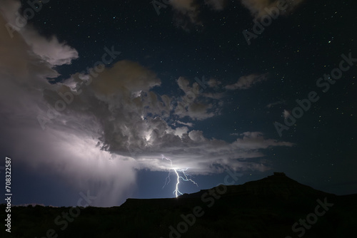 Fototapet A summer monsoon storm delivers one of it's last lightning bolts as it passes into the distance beyond Gooseberry Mesa in Southern Utah, USA, leaving a starry night sky washed clean of dust