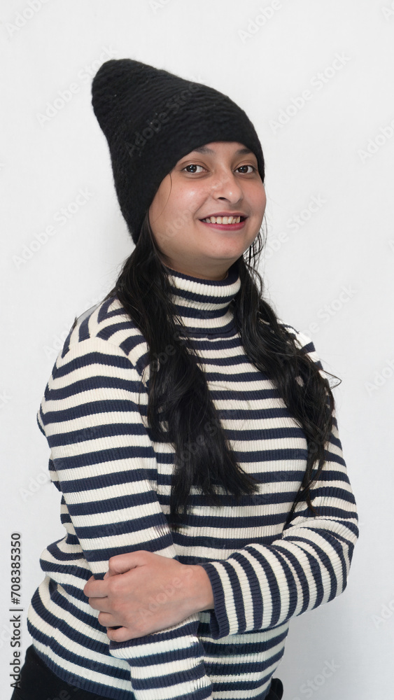 Cold season a young Indian girl with a smiling face wearing a black woolen cap and having turtleneck black and white striped sweater, isolated white background. Cold season a young Indian girl with a smiling face wearing a black woolen cap and having turtleneck black and white striped sweater, isolated white background.