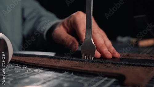 Close up of tanner hands making holes in leather purse using line piercer and hammer