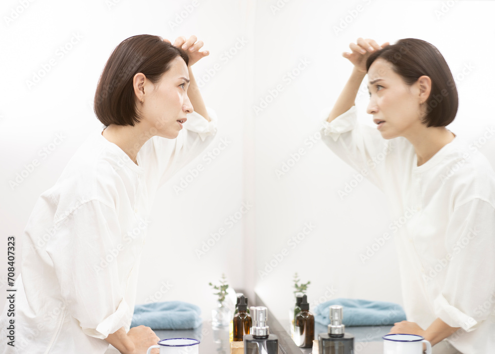 ヘアケア/不安な表情で鏡を見ながら髪を触るミドル世代女性 ヘアケア/不安な表情で鏡を見ながら髪を触るミドル世代女性