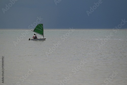Petit bateau avec une voile verte seul au milieu de l'océan.