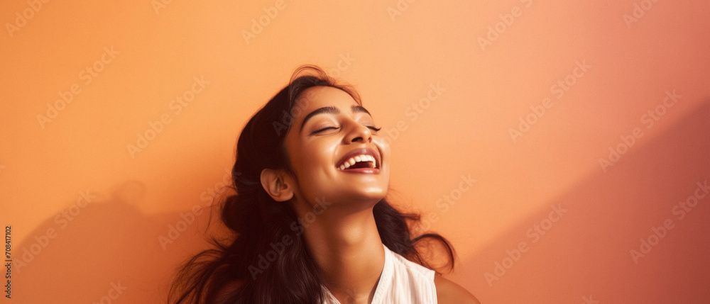 Fototapeta premium Portrait of a beautiful young indian woman laughing against orange wall