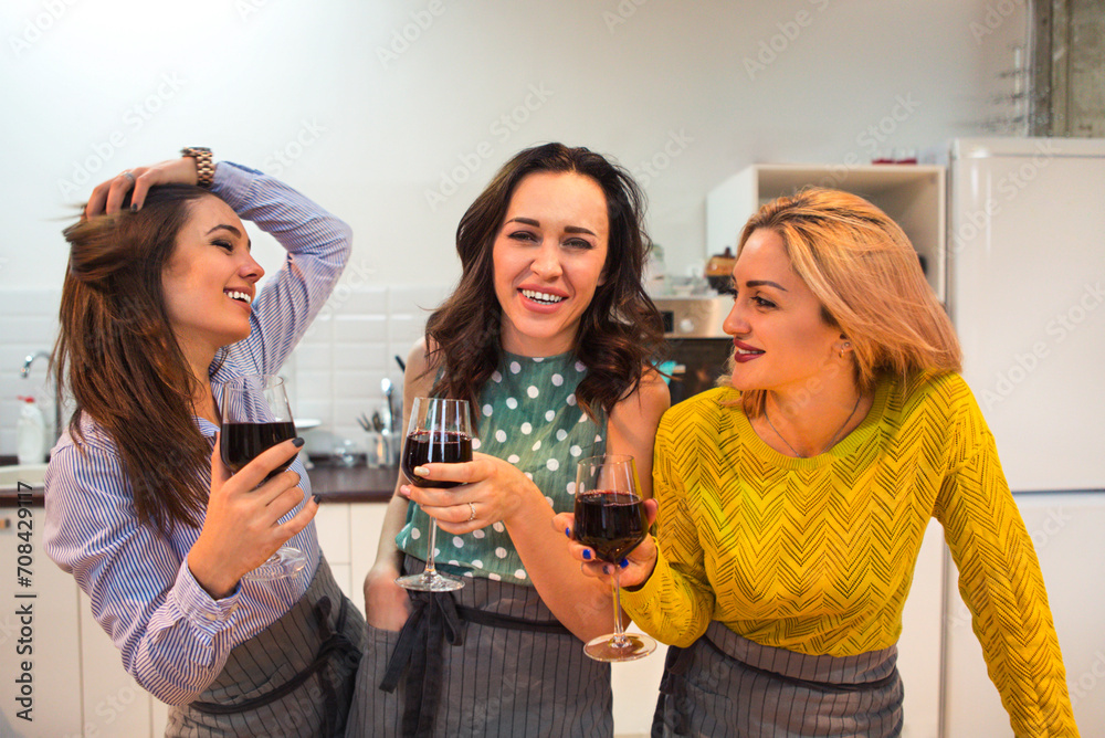 Cheerful friends preparing a meal together and drinking red wine in the kitchen Cheerful friends preparing a meal together and drinking red wine in the kitchen