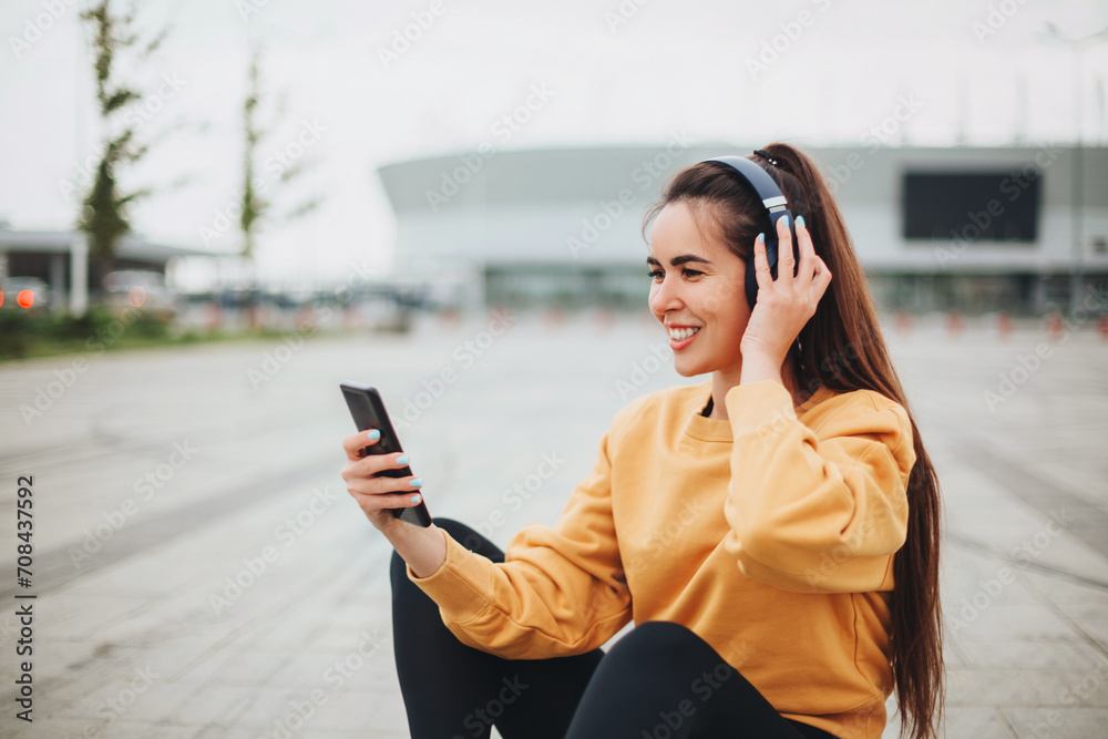 Outdoor photo of happy young woman in headphones listening to music on smartphone Outdoor photo of happy young woman in headphones listening to music on smartphone