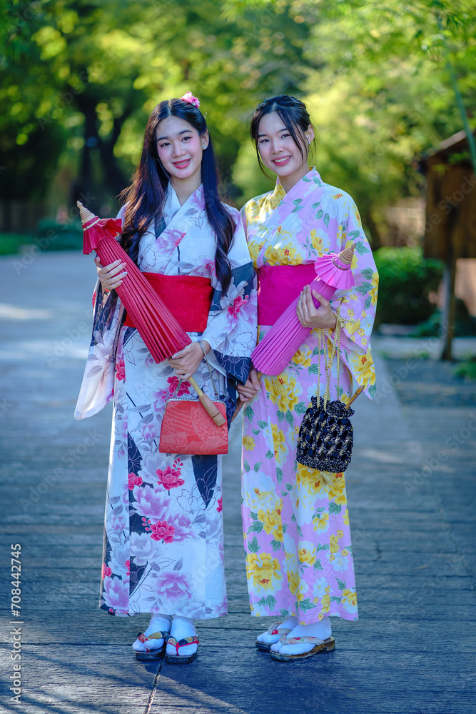 Pretty the Traveller Young Asian woman wearing a Japanese traditional kimono dress, a Yukata dress, and holding an umbrella is happy and cheerful in the green natural park.