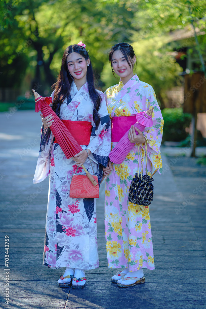 Pretty the Traveller Young Asian woman wearing a Japanese traditional kimono dress, a Yukata dress, and holding an umbrella is happy and cheerful in the green natural park.