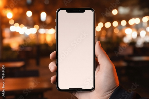 Male hand holds a smartphone with a white screen on the background of a restaurant