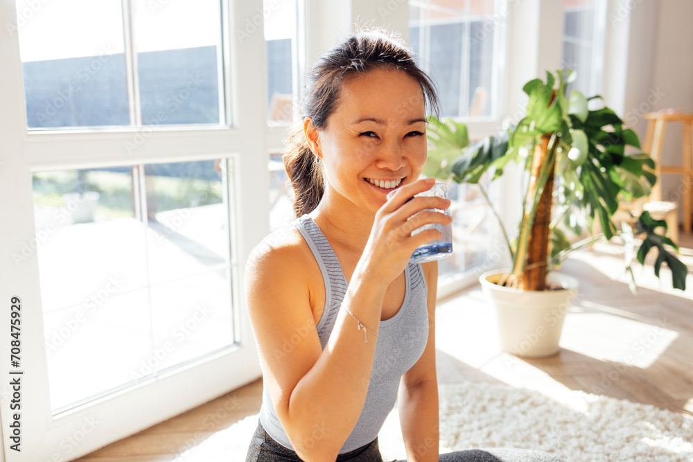 Asian woman drink water after yoga in the living room of her house Asian woman drink water after yoga in the living room of her house