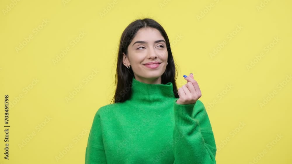 Playful Caucasian woman forms a heart shape with fingers, radiating a sense of affection and joy. The vibrant contrast of the heart gesture against the yellow background adds a visual charm.
