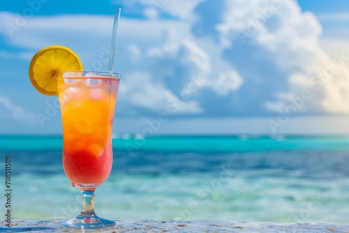 A colorful tropical drink garnished with an orange slice sits on a wooden ledge in front of a blue ocean.